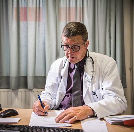 Dokter met witte jas, bril en stethoscoop vult document in