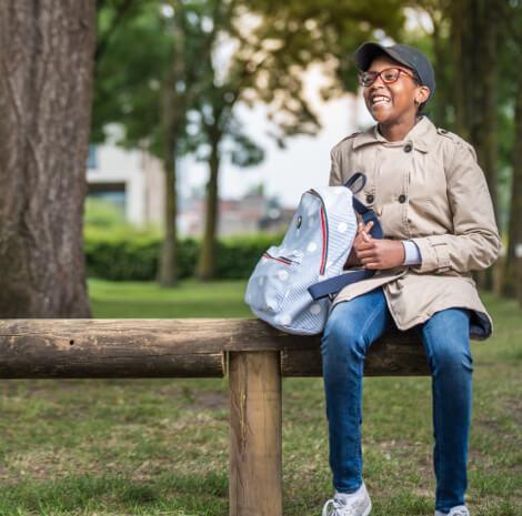 Meisje met bril en rugzak zit op bank en lacht