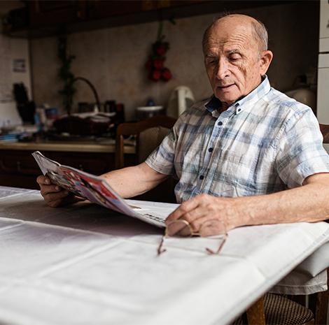 Oudere man zit aan tafel en leest de krant