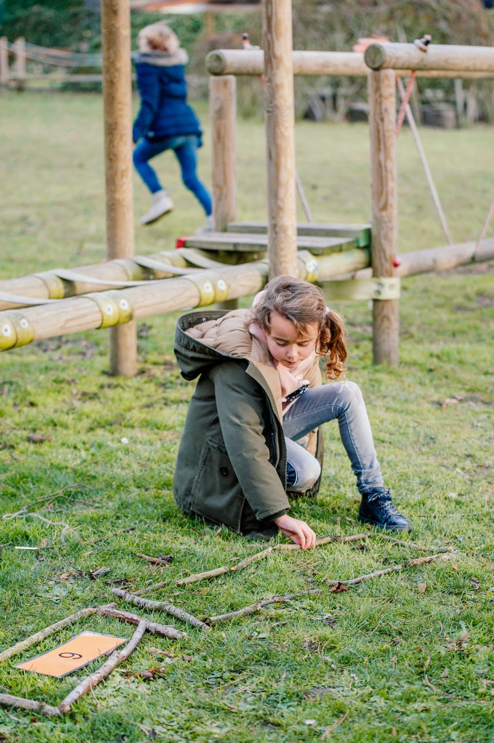 Kind leert buiten, met takjes in het groen 