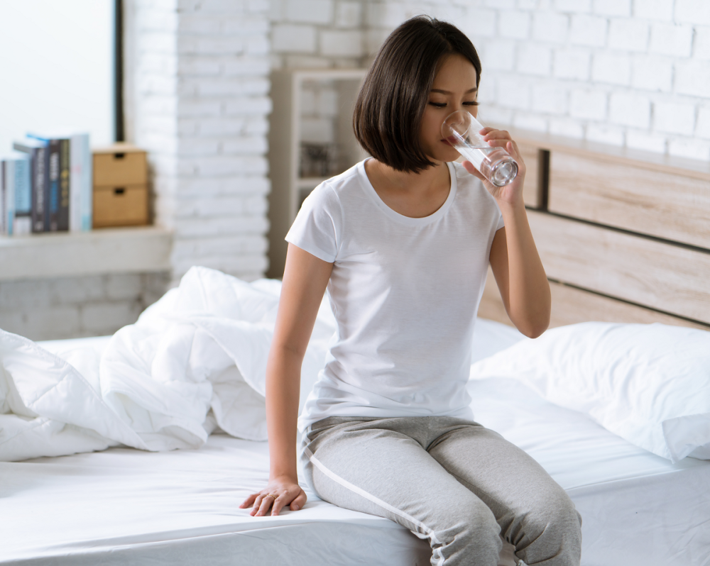 Vrouw zit op bed en drinkt een glas water 