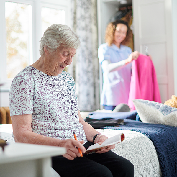 Oma al zittend op haar bed met verzorgster achter haar