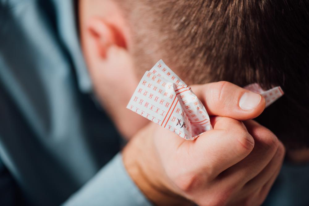 man zit voorovergebogen met verfrommeld loterij ticket
