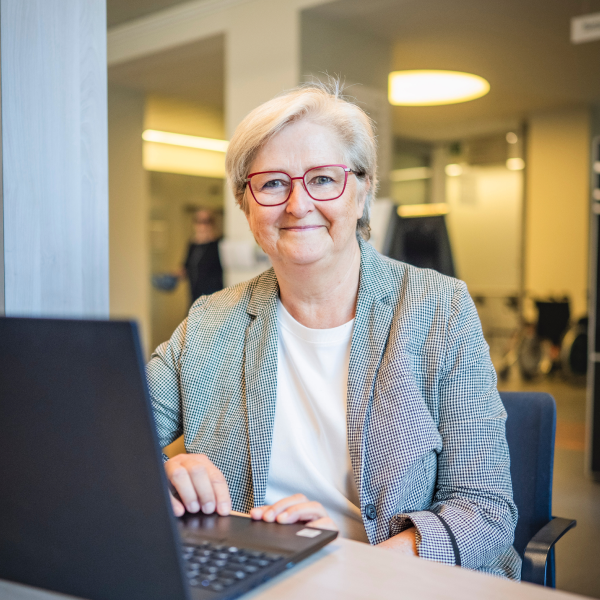Gina zit voor een laptop en kijkt in de lens